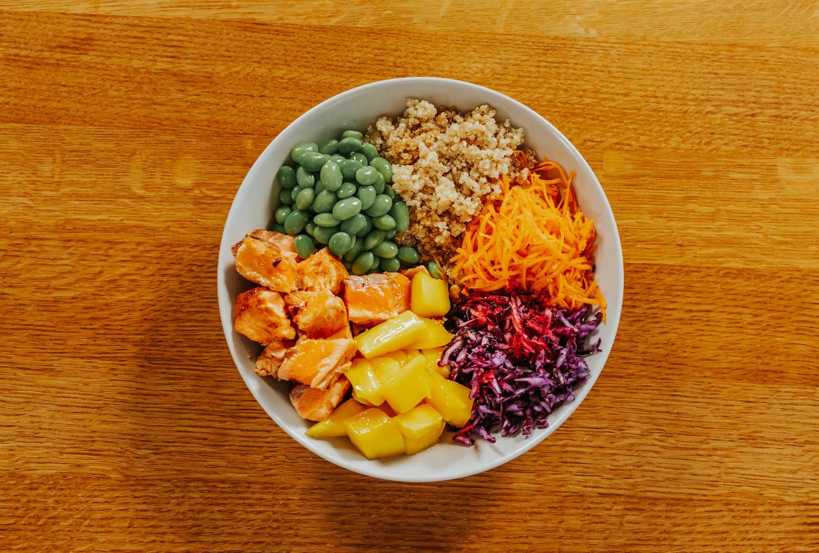 Salmon poke bowl with quinoa, edamame, carrot, cabbage, and mango