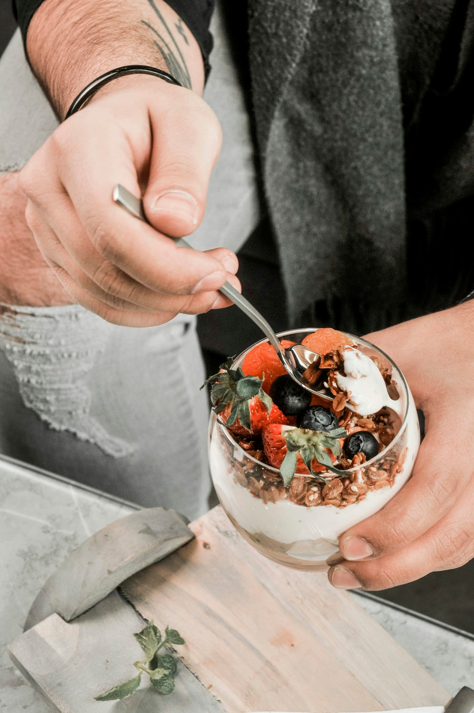Person eating a yogurt parfait with granola, strawberries, and blueberries
