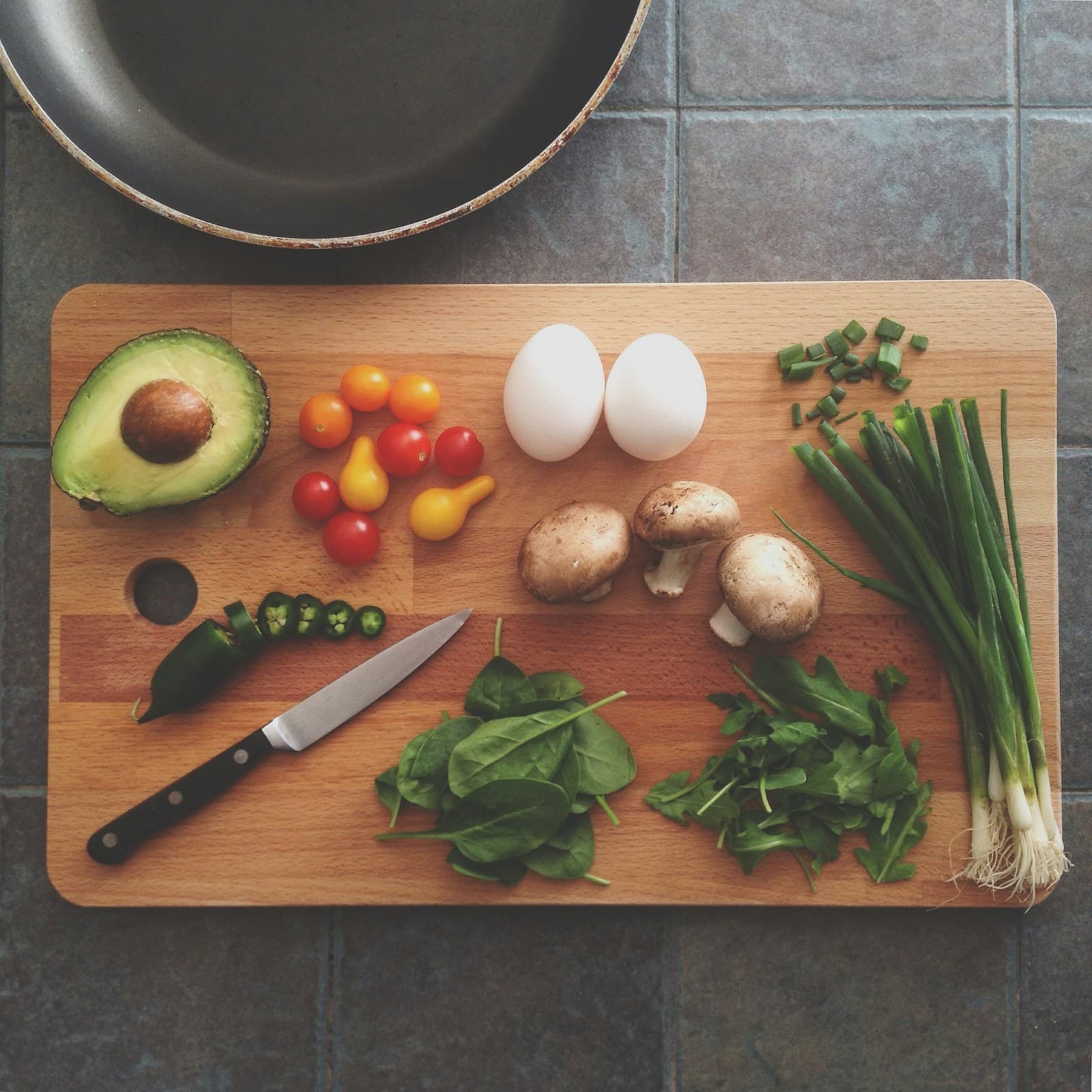 Avocado, eggs, mushrooms, tomatoes, spring onions, and greens on a cutting board